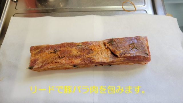 スパイス塩をすり込んだスペイン産の豚バラ肉を、リードに包んでいる写真。