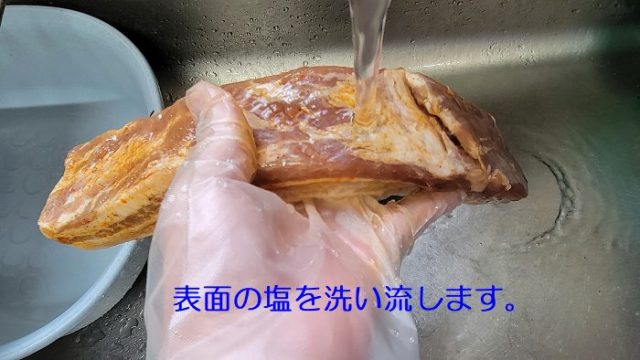 塩漬けした豚バラ肉の表面に着いた塩を洗い流している写真。