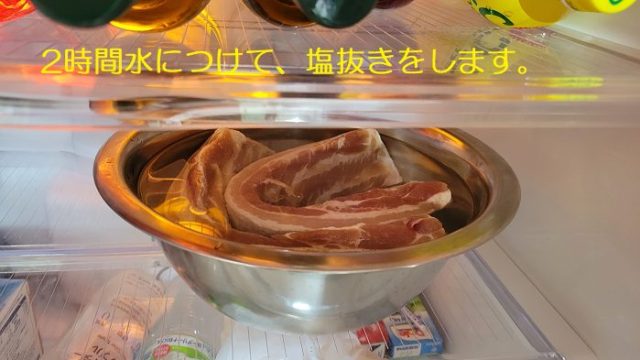 水を入れたボールに豚バラ肉を入れて、冷蔵庫の中で塩抜きをしている写真。